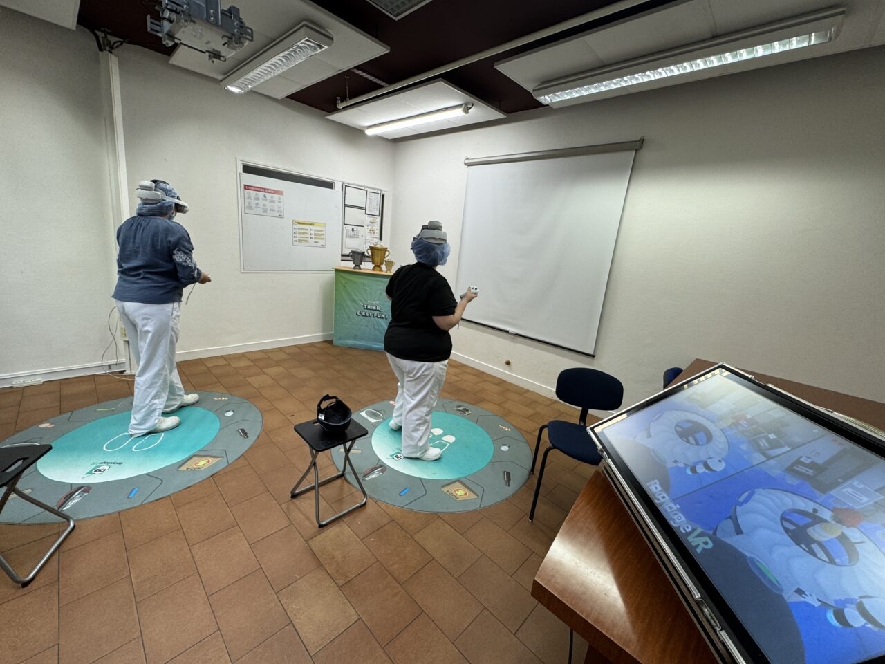Deux personnes utilisent des casques VR sur des tapis, avec un écran au premier plan